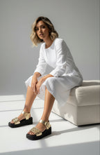 Modelo usando la Plataforma Aurea Comodidad EVA con Acabado Oro, sentada en un sofá con vestido blanco.