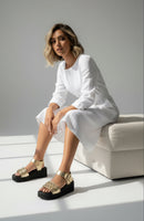 Modelo usando la Plataforma Aurea Comodidad EVA con Acabado Oro, sentada en un sofá con vestido blanco.